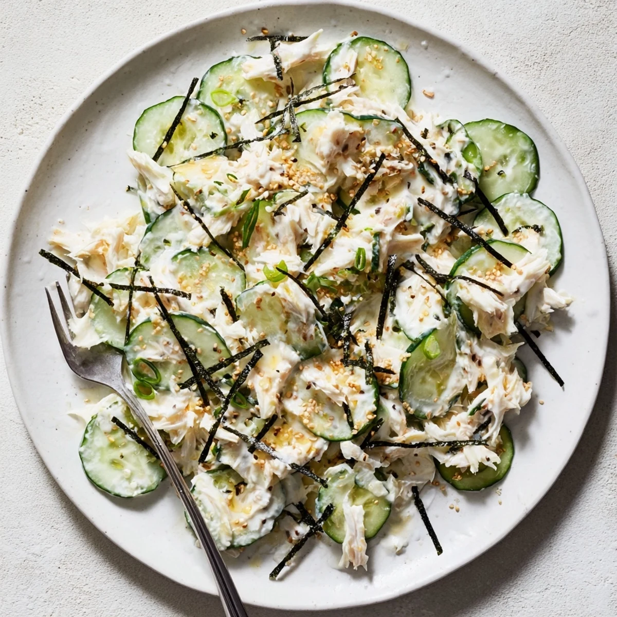 Fresh California Roll Cucumber Salad topped with pickled ginger, nori, and sesame seeds, served in a white ceramic bowl.