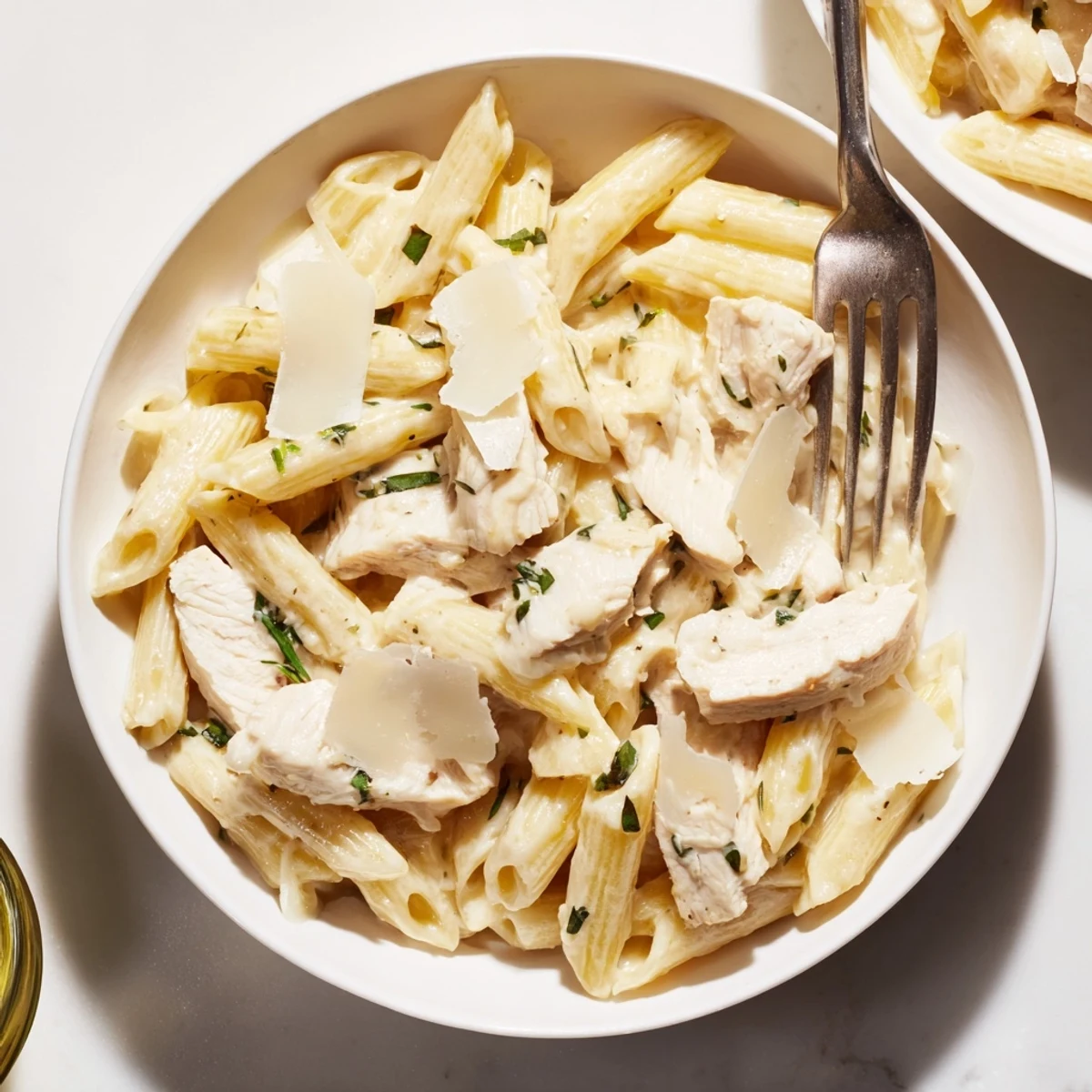 Roasted Garlic Chicken Penne is garnished with parsley and Parmesan, served in a white bowl with a side salad for a balanced family dinner.