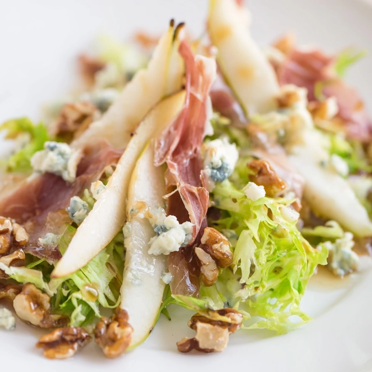 A close-up of the frisée, pear, and blue cheese salad shows juicy pears, rich cheese, and crispy prosciutto atop fresh greens with glistening vinaigrette.