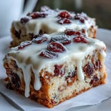Frosted Cranberry Bliss Bars topped with zesty orange cream cheese swirls and melted white chocolate drizzle on a platter.
