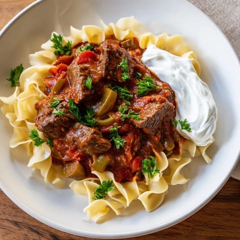 A bowl of hearty Hungarian Goulash with tender beef, served generously over buttery egg noodles.