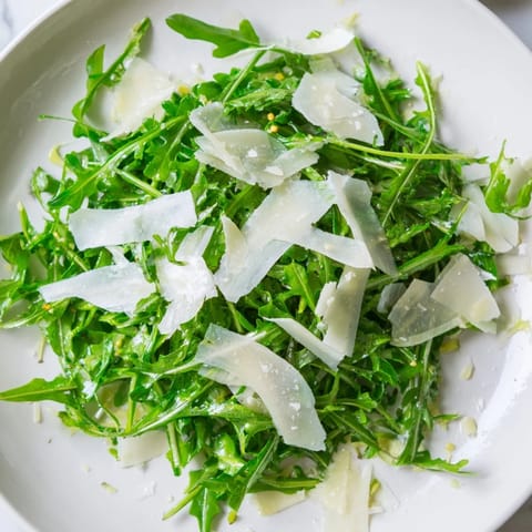 Arugula salad with lemon dressing, looking fresh, with Parmesan cheese and shallots.