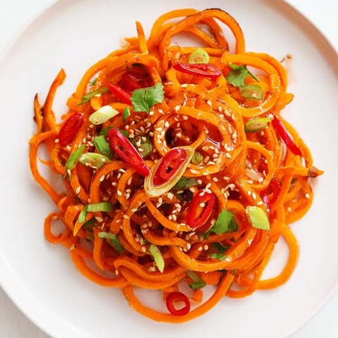 A close-up of Carrot Ribbon Salad Asian-Style featuring spiralized carrots, lime wedges, and fresh cilantro for a bright, refreshing side dish.