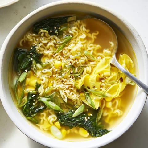 A comforting bowl of Elevated Ramen Egg Drop Soup topped with scallions and sesame seeds beside steaming chopsticks.