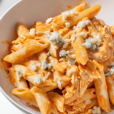 A close-up of Buffalo Chicken Pasta garnished with fresh chives, served steaming in a rustic bowl.
