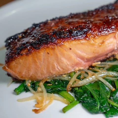 A close-up of caramelized miso salmon resting on tender spinach with fresh ginger and sesame seeds.  