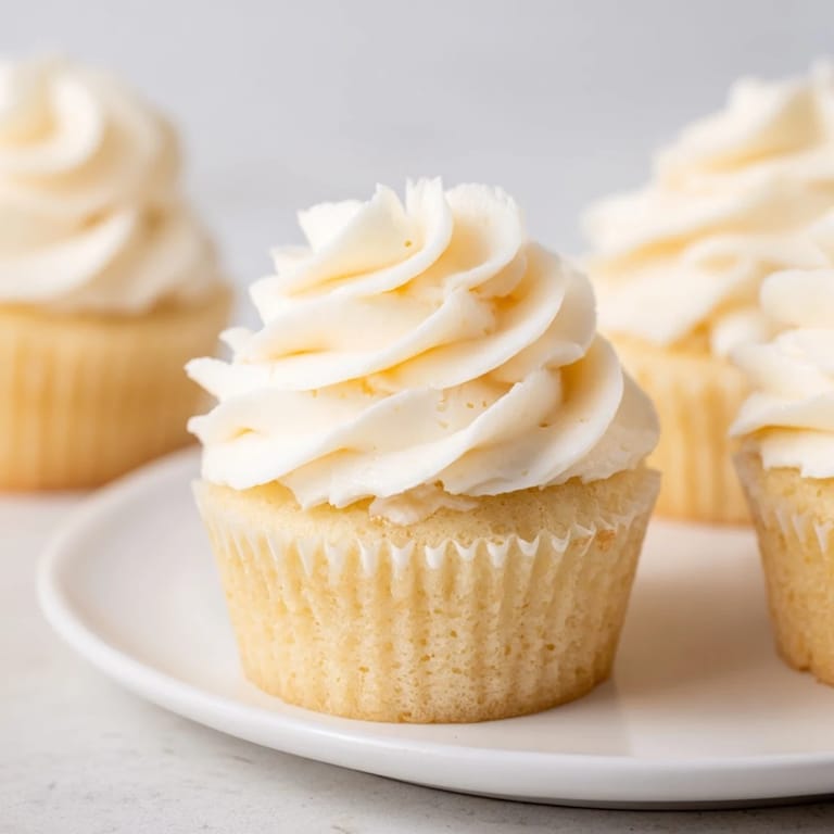 Close-up of freshly baked vanilla cupcakes, showcasing a swirl of creamy buttercream frosting, delicious dessert.