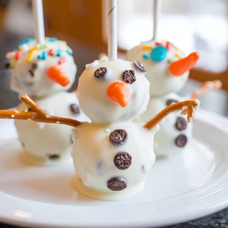 Festive Oreo Snowman Cake Pops, decorated with chocolate chips and pretzel arms for a delightful dessert.