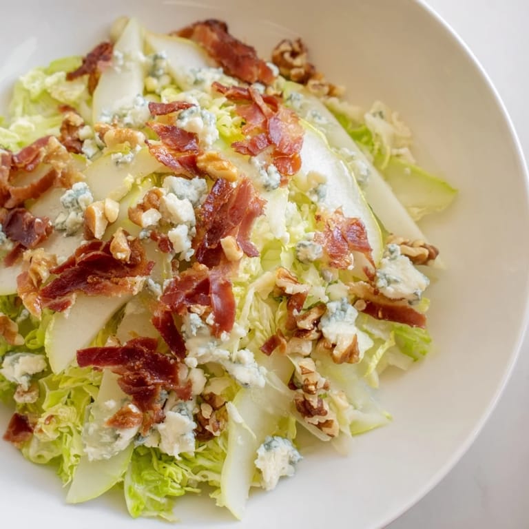 Golden pear slices mingle with bitter frisée and crumbled blue cheese in this vibrant salad, finished with crunchy walnuts and shards of crispy prosciutto.